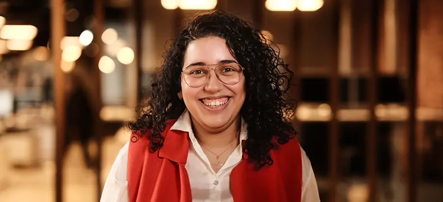 Jonge vrouw met bos krullen staat in een Persoonality vestiging en kijkt lachend in de camera