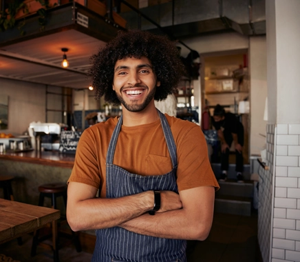 Man staat met armen over elkaar, heeft een keukenshirt aan en lacht 