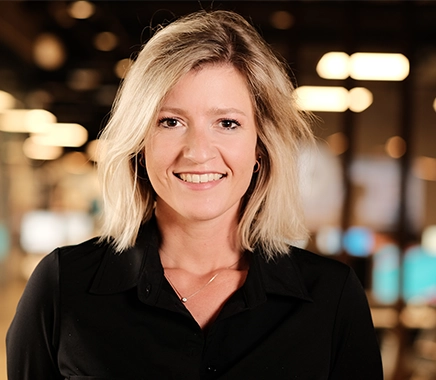 Jonge vrouw met kort blond haar. Ze heeft een zwarte blouse aan en kijkt in de camera en lacht.