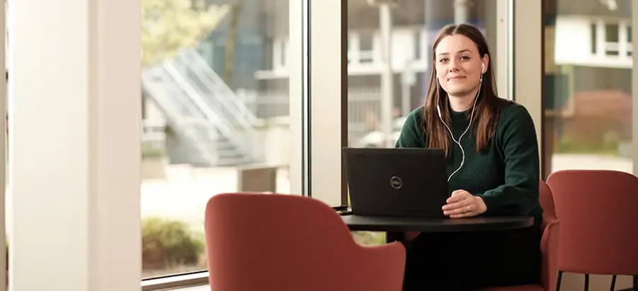 Jonge mevrouw met lang bruin haar zit achter een laptop en lacht