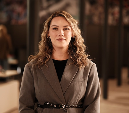 Jonge vrouw met donker blond lang krullend haar kijkt lachend in de camera met op de achtergrond een Persoonality vestiging