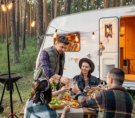 Groep jonge vrienden zitten voor de caravan en genieten buiten van een diner 